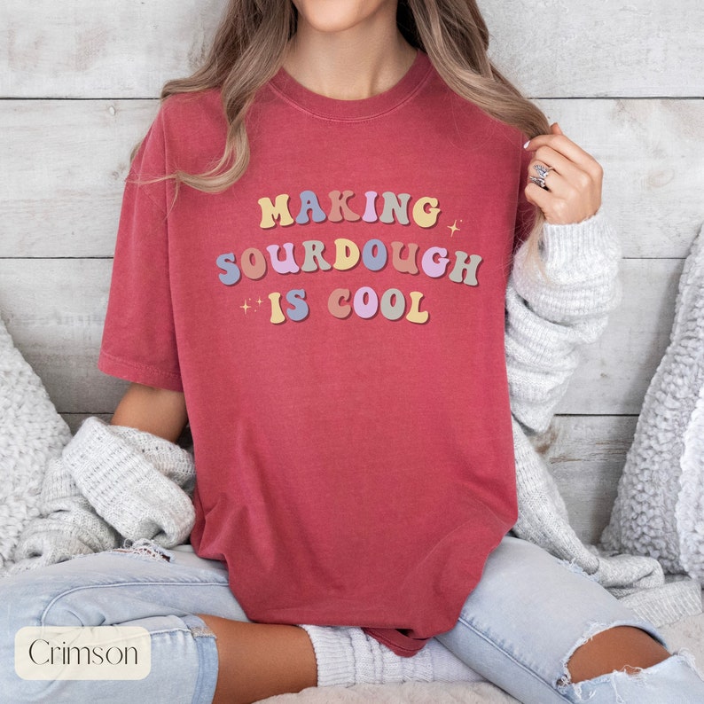 Peut inclure: Un t-shirt rouge avec le texte "MAKING SOURDOUGH IS COOL" en lettres color&eacute;es de style r&eacute;tro.