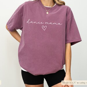 K&ouml;nnte beinhalten: Ein mauvefarbenes T-Shirt mit dem Text "dance mama" und einer Herzgrafik in Wei&szlig;.
