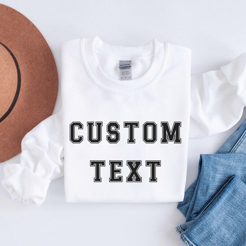 Peut inclure: Sweat-shirt blanc avec un texte noir qui dit "CUSTOM TEXT" dans une police de caract&egrave;res de style universitaire.