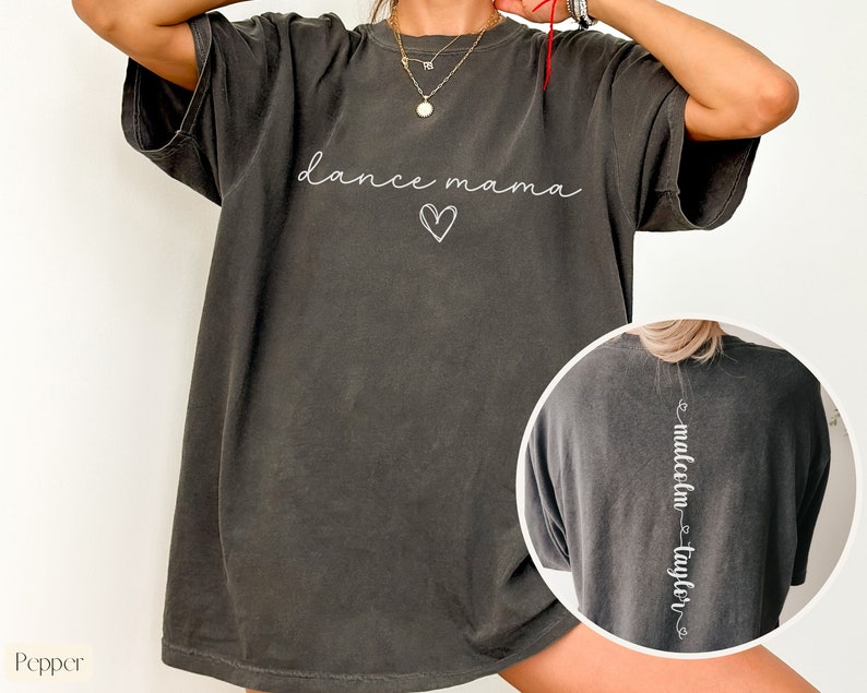 K&ouml;nnte beinhalten: Ein &uuml;berdimensioniertes, dunkelgraues T-Shirt mit dem Text "dance mama" und einem Herz auf der Vorderseite. Die R&uuml;ckseite des Shirts tr&auml;gt den Text "malcolm - taylor" vertikal auf dem R&uuml;cken.