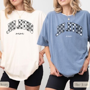 Pu&ograve; includere: Due magliette a maniche corte, una avorio e una blu jeans, con la scritta "Jiu Jitsu" in un disegno a scacchi. La maglietta avorio ha "mama" sotto, e la maglietta blu jeans ha "mom". Entrambe le magliette sono abbinate a pantaloncini neri.