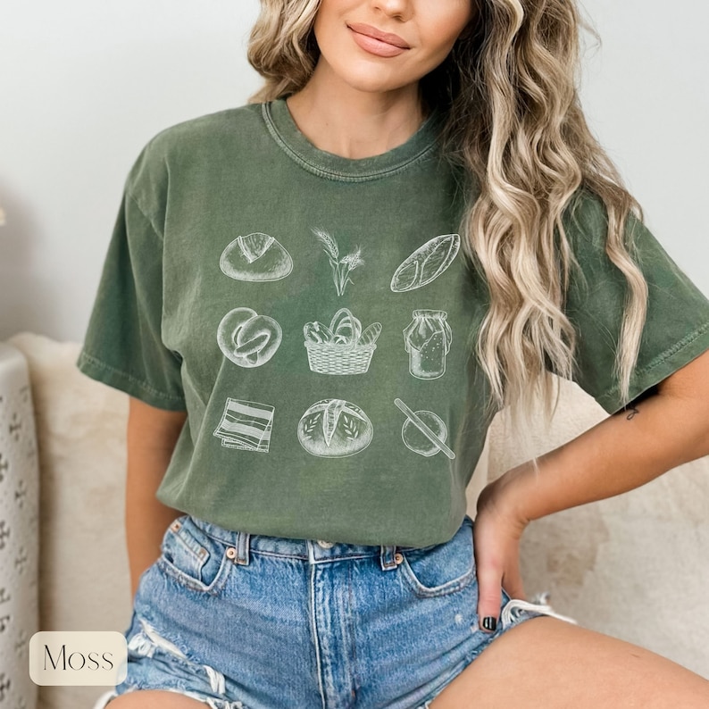 Peut inclure: Un t-shirt vert avec un motif blanc de diff&eacute;rents pains et articles de boulangerie. Le motif comprend un pain, un bretzel, un panier de pain, un pot de levain, un rouleau &agrave; p&acirc;tisserie et une tige de bl&eacute;.