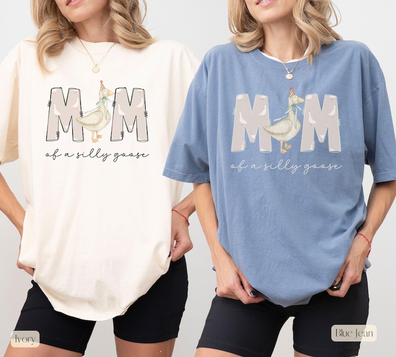 Puede incluir: Dos camisetas con el texto "MOM of a silly goose" y un ganso de dibujos animados con un gorro de fiesta. La camiseta de la izquierda es de color marfil y la camiseta de la derecha es de color azul vaquero.