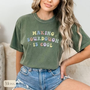 Peut inclure: Un t-shirt vert avec le texte "Making sourdough is cool" en lettres color&eacute;es.