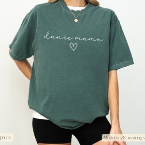 K&ouml;nnte beinhalten: Ein &uuml;berdimensioniertes T-Shirt in Tealblau mit dem Text "dance mama" in wei&szlig;er Schrift mit einem darunter gezeichneten Herzen.