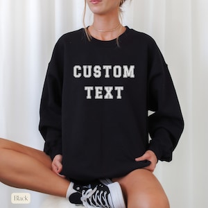 Peut inclure: Sweat-shirt noir avec le texte "CUSTOM TEXT" en blanc.