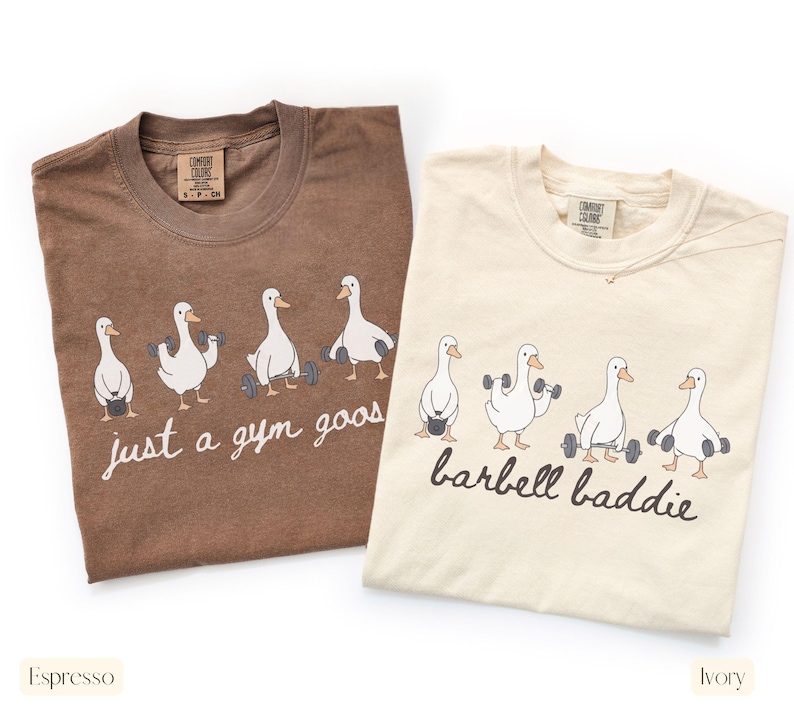 K&ouml;nnte beinhalten: Zwei T-Shirts, eines in Espresso und eines in Elfenbein, mit Rundhalsausschnitt. Das Espresso-Shirt hat den Text "just a gym goos" und das elfenbeinfarbene Shirt den Text "barbell baddie". Beide Shirts zeigen eine Grafik von G&auml;nsen, die Gewichte heben.