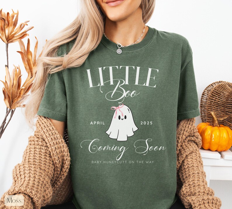 Op de afbeelding: Groen t-shirt met de tekst "LITTLE Boo" en een cartoon spookje met een roze strik. Op het shirt staat ook "April 2025" en "Coming Soon". De woorden "Baby Huneycutt on the way" staan ook op het shirt.