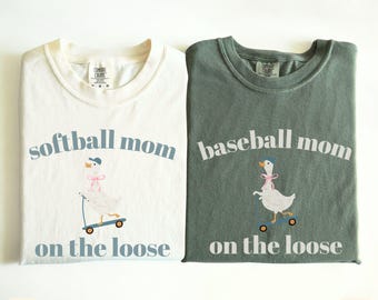 May include: Two t-shirts, one ivory and one moss green, with a graphic of a goose riding a scooter. The ivory shirt says "softball mom on the loose" and the green shirt says "baseball mom on the loose".