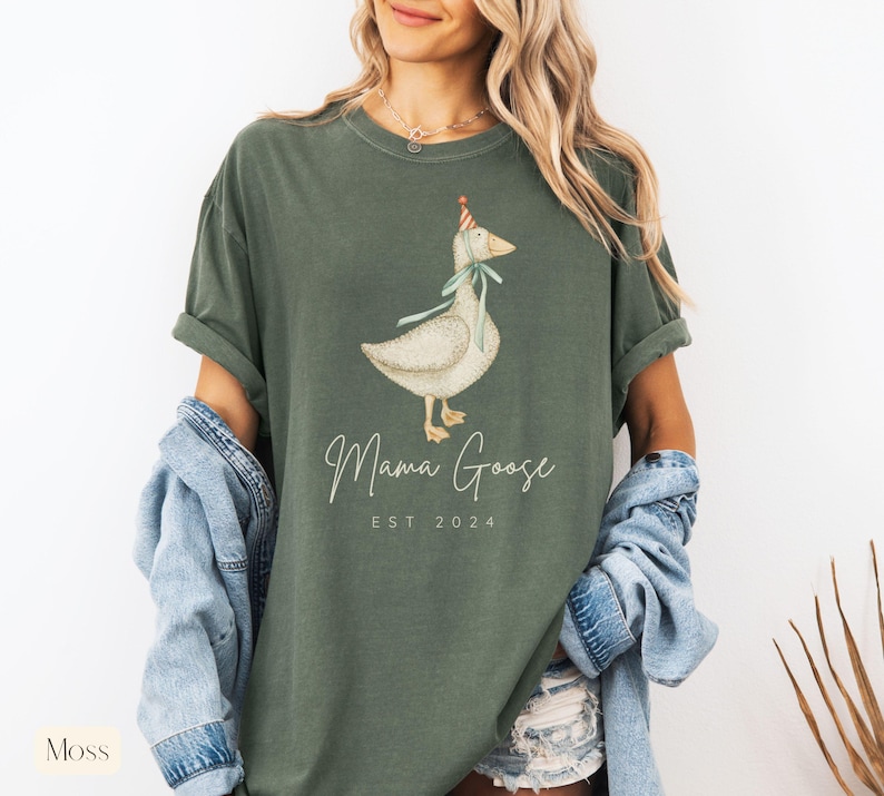 May include: A green t-shirt with a white goose wearing a party hat and the text "Mama Goose Est 2024".