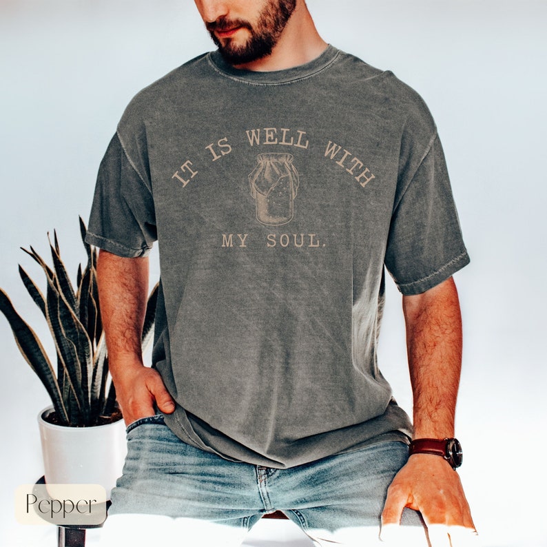 Puede incluir: Una camiseta gris con un aspecto vintage que presenta el texto "It is well with my soul." y un dibujo de un tarro de cristal.