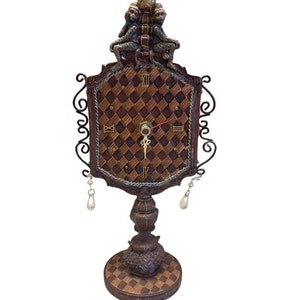 May include: A brown and gold tabletop clock with a checkered design and three monkeys on top. The clock has a Roman numeral face and a black metal frame.