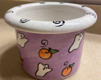 May include: A purple ceramic candy dish with a white rim and black swirl design. The dish is decorated with orange pumpkins and white ghosts.
