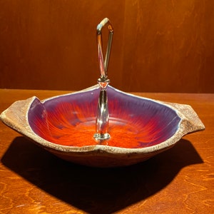 May include: A purple and orange ceramic serving dish with a silver handle. The dish has a textured surface and a unique design.