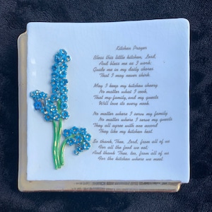 Può includere: Una placca di ceramica bianca con un motivo floreale blu e verde e una poesia su una preghiera in cucina. La poesia recita: "Benedici questa piccola cucina, Signore, E benedici me mentre lavoro; Guidami nelle mie faccende quotidiane Affinché io non trascuri mai. Possa mantenere la mia cucina allegra Non importa cosa cucino, Che la mia famiglia e i miei ospiti Amino ogni angolo. Non importa dove servo la mia famiglia Non importa dove servo i miei ospiti Sono tutti d'accordo Gli piace la mia cucina. Quindi grazie, Signore, da parte di tutti noi Per tutto il cibo che mangiamo; E grazie anche a te, da parte di tutti noi Per la cucina dove ci incontriamo."