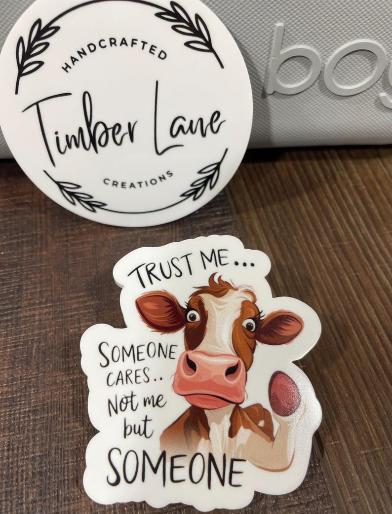 May include: White sticker with a brown and white cow illustration. The cow has a pink nose and is looking at the viewer. The text on the sticker reads "Trust me... Someone cares... Not me but Someone".