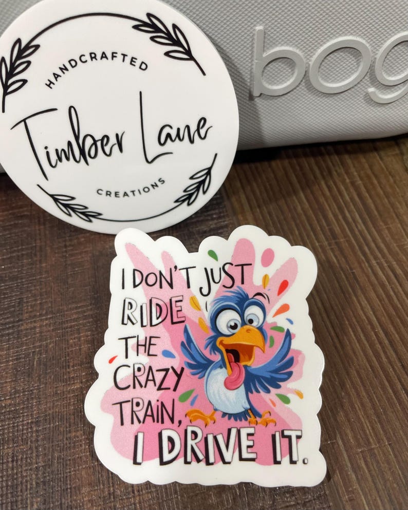 May include: A white sticker with a pink background and a cartoon blue bird with a red tongue. The text on the sticker reads "I don't just ride the crazy train, I drive it."