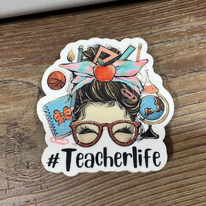May include: White sticker with a cartoon illustration of a woman with a messy bun, wearing glasses and surrounded by school supplies. The text "#Teacherlife" is below the illustration.
