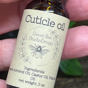 May include: A small brown glass bottle of cuticle oil. The label reads "Cuticle oil" with "Sweet Bee Studio Design" and a bee illustration. Ingredients include Sweet Almond Oil, Castor Oil, and Vitamin Oil. Net weight is .5 oz.