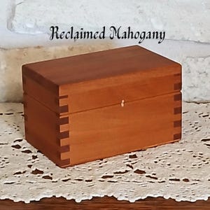 May include: A rectangular wooden box crafted from reddish-brown mahogany with visible finger joints at the corners. The lid is flat and sits flush with the base. The text Reclaimed Mahogany is printed in a black script font above the box.