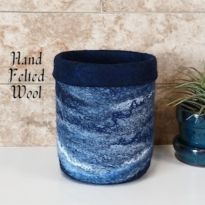 May include: A hand felted wool planter in a blue and white marbled design with a dark blue rim.  The planter is sitting on a white surface.