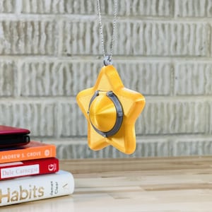 May include: A gold star-shaped pendant with a silver center, hanging from a silver chain. The pendant is a 3D printed replica of a popular video game item.
