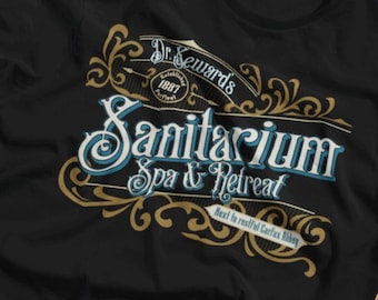 Könnte beinhalten: Schwarzes T-Shirt mit einem Grafikdesign im Vintage-Stil mit dem Text "Dr. Seward's Sanitarium Spa & Retreat" in Gold- und Blautönen. Der Text "Next to restful Carfax Abbey" ist ebenfalls enthalten.