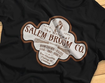 Könnte beinhalten: Schwarzes T-Shirt mit einem braunen und weißen Vintage-Logo für Salem Broom Co. Das Logo zeigt eine Hexe auf einem Besen und den Text "ESTD. 1692 The Original Salem Broom Co."