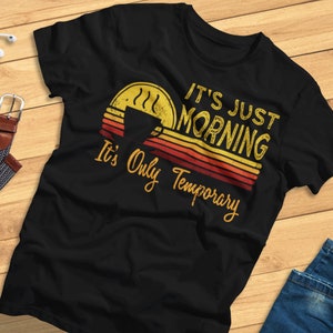 Puede incluir: Camiseta negra con un gráfico de estilo vintage que dice "It's Just Morning It's Only Temporary" con una taza de café y un diseño de amanecer.