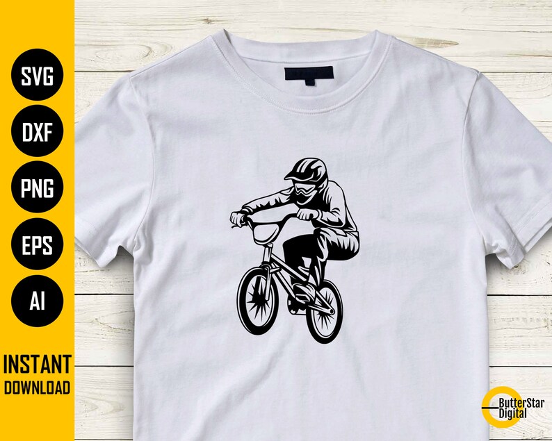 Op de afbeelding: Wit t-shirt met een zwarte afbeelding van een BMX-fietser in actie. Het ontwerp toont een helm en een bril. De linkerkant van het shirt heeft de tekst "SVG, DXF, PNG, EPS, AI" en "DIRECT DOWNLOADEN".