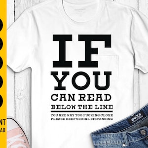 Könnte beinhalten: Weißes T-Shirt mit schwarzem Aufdruck: „IF YOU CAN READ BELOW THE LINE YOU ARE WAY TOO FUCKING CLOSE PLEASE KEEP SOCIAL DISTANCING“. Das Shirt hat eine Tasche und wird mit einer blauen Jeans kombiniert.