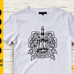 May include: White t-shirt featuring a black graphic of a skeletal hand giving the middle finger, surrounded by floral elements. The word "NEGATIVITY" is displayed on a banner below the hand. The shirt also has the words "SVG, DXF, PNG, EPS, AI" and "INSTANT DOWNLOAD" on the left side.