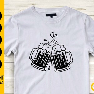 May include: White t-shirt featuring a black graphic of two beer mugs clinking together, with overflowing foam. The design is a simple, bold illustration. The words "INSTANT DOWNLOAD" are printed on the left side of the shirt.