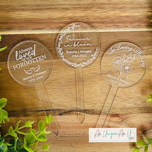 May include: Three clear acrylic memorial garden stakes with engraved text. One reads "Always Loved, Never Forgotten" with a name and dates. Another says "Forever in bloom" with a name and dates. The third says "In Loving Memory" with a name and dates.