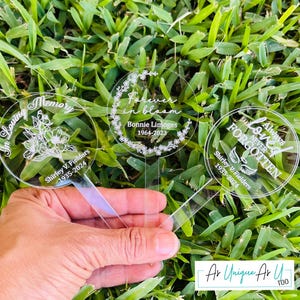 May include: Three clear acrylic memorial garden stakes with engraved text and floral designs. One reads "In Loving Memory," another "Forever in bloom," and the third "Always Loved Never Forgotten." Each includes a name and dates.