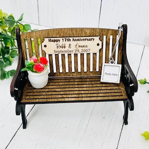 May include: A wooden miniature bench with a personalized plaque that reads "Happy 17th Anniversary Robb & Connie September 29, 2007". A small white picture frame hangs from the back of the bench with the words "Photo Here" printed on it.