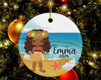 Puede incluir: Adorno navideño redondo de cerámica con una niña de dibujos animados con falda de hierba y corona de flores en una escena de playa. El nombre "Emma" y el año "2025" están impresos. El adorno cuelga de un árbol de Navidad.