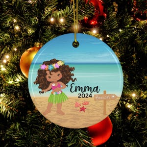 May include: A round ceramic Christmas ornament featuring a cartoon girl with brown hair wearing a flower lei and a green grass skirt. The girl is standing on a beach with a blue ocean and sky in the background. The ornament also includes the text "Emma 2024 Beach".