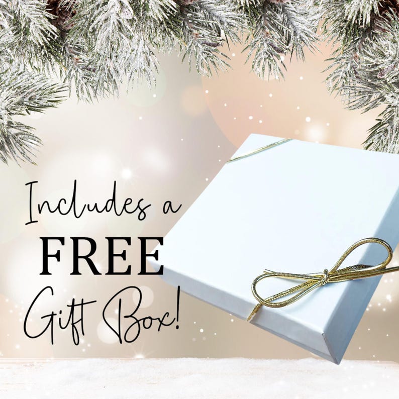 May include: A white gift box with a gold ribbon bow. The box is sitting on a white surface with a snowy pine branch in the background. The text "Includes a FREE Gift Box!" is written in black on a white background.