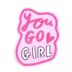 Puede incluir: Parche de fieltro rosa con el texto "You Go Girl" en letras rosa y blancas con un pequeño corazón rosa.