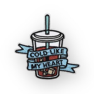 May include: An embroidered patch with a cartoon image of a cold drink in a clear cup with a straw and ice cubes. The text "COLD LIKE MY HEART" is on a blue ribbon wrapped around the cup.