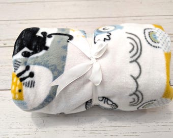 May include: A white fleece baby blanket with a yellow, gray, and black print of animals and clouds. The blanket is tied with a white ribbon.