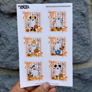 May include: A white sticker sheet titled 010 Sensational 6 Halloween featuring six rectangular designs with orange striped backgrounds, spiderwebs, and bows. Each design shows a cartoon ghost character wearing different accessories and holding pumpkins.