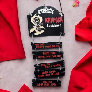 May include: A black wooden sign with the text "WELCOME KRUEGER Residence" and a graphic of Freddy Krueger. Below the sign are five smaller signs with text about Freddy Krueger's arrival.