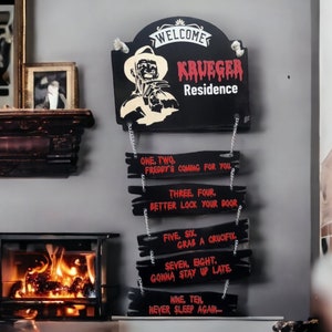 May include: A black wooden sign with a red and white illustration of Freddy Krueger, the character from the Nightmare on Elm Street horror films. The sign reads "Welcome Krueger Residence" and has a series of smaller signs hanging below it with the text "One, Two, Freddy's coming for you", "Three, Four, Better lock your door", "Five, Six, Grab a crucifix", "Seven, Eight, Gonna stay up late", "Nine, Ten, Never sleep again..."