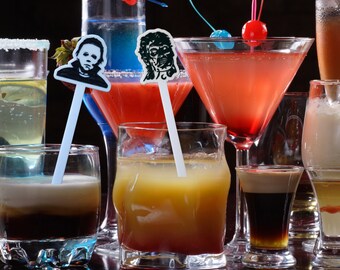 Può includere: Una varietà di cocktail in bicchieri diversi con mescolatori per bevande a tema Halloween. I mescolatori presentano immagini di personaggi di film horror.