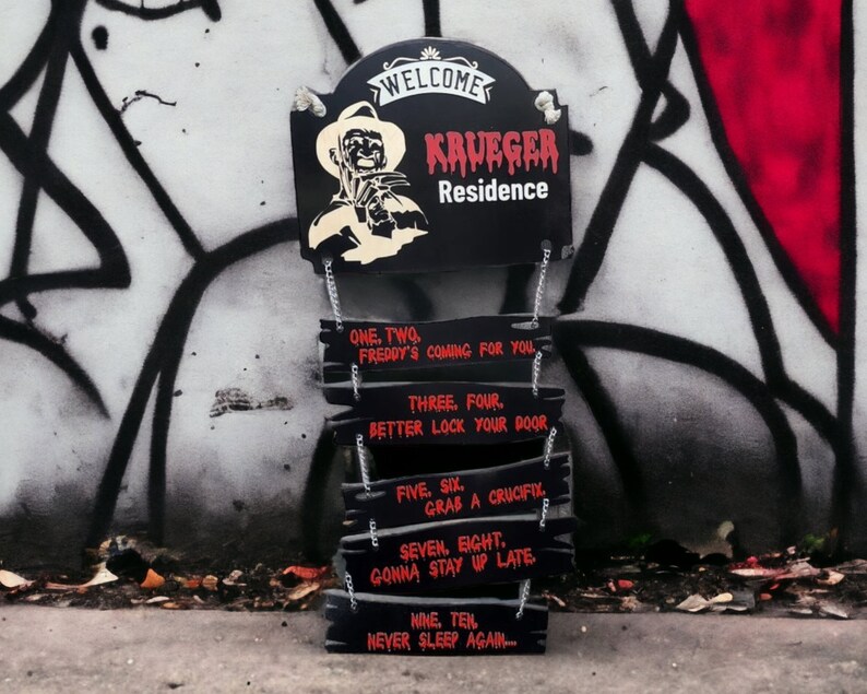 May include: Black and red wooden sign with the text "WELCOME KRUEGER Residence" and a graphic of Freddy Krueger. The sign is hanging from chains and has several smaller signs hanging below it with the text "ONE. TWO. FREDDY'S COMING FOR YOU", "THREE. FOUR. BETTER LOCK YOUR DOOR", "FIVE. SIX. GRAB A CRUCIFIX", "SEVEN. EIGHT. GONNA STAY UP LATE", and "NINE. TEN. NEVER SLEEP AGAIN..."
