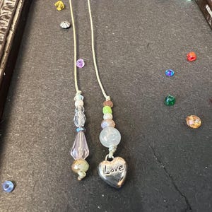 May include: Two beaded necklaces with a heart charm that says "Love". One necklace has pink and clear beads, the other has green, pink, and white beads.