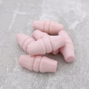 May include: A group of five pink plastic toggle buttons. The buttons are shaped like a milk carton and have a ribbed texture.