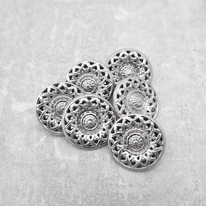 May include: A set of seven silver-toned buttons with intricate, circular designs. The buttons have a raised, textured surface and a shiny finish.
